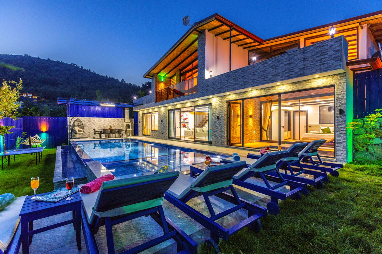 Beautiful modern villa with a well-lit swimming pool and deck chairs in a serene outdoor setting.