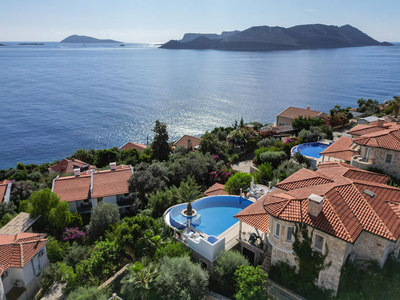 Aerial view of coastal Mediterranean villas with infinity pools overlooking the sea.
